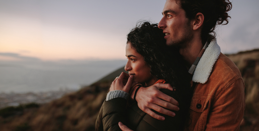 Side view of affectionate couple embracing and looking away. Man and woman together on mountain looking at a view.